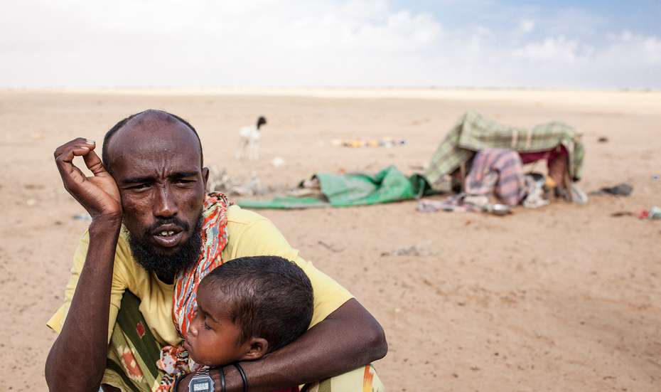 Ihre Hilfe für Somalia. Bildbeschreibung: Ein erschöpft aussehender Mann und ein Kleinkind hocken in einer Wüstenlandschaft. 