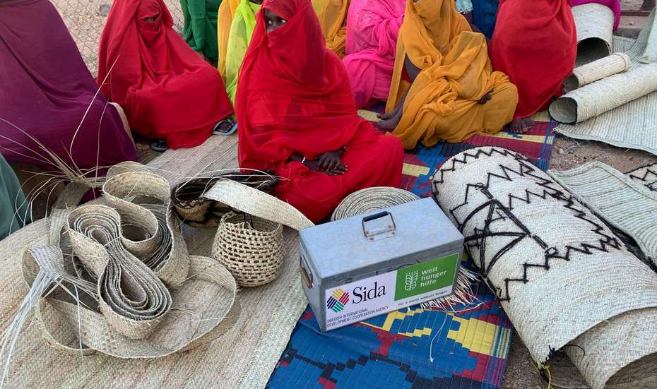Frauen in einem Camp für Binnenflüchtlinge in Port Sudan. Mehrere Frauen in bunter Kleidung sitzen auf geflochtenen Matten auf dem Boden.