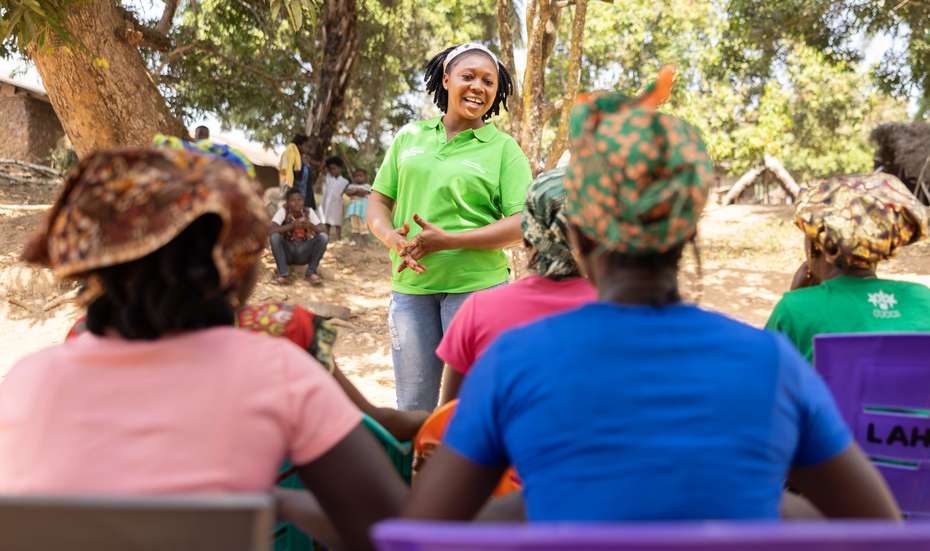 Im Dorf Giehun in Sierra Leone unterrichtet Welthungerhilfe-Mitarbeiterin Hannah Massah Jaward eine Gruppe junger Frauen und einen jungen Mann draußen unter Bäumen.