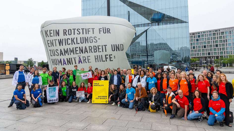 Gruppenfoto mehrerer Dutzend Menschen von verschiedenen Hilfsorganisationen auf einem Platz in Berlin. Sie stehen vor einem großen Transparent mit der Aufschrift „Kein Rotstift bei Etats für Entwicklungszusammenarbeit und Humanitäre Hilfe“.