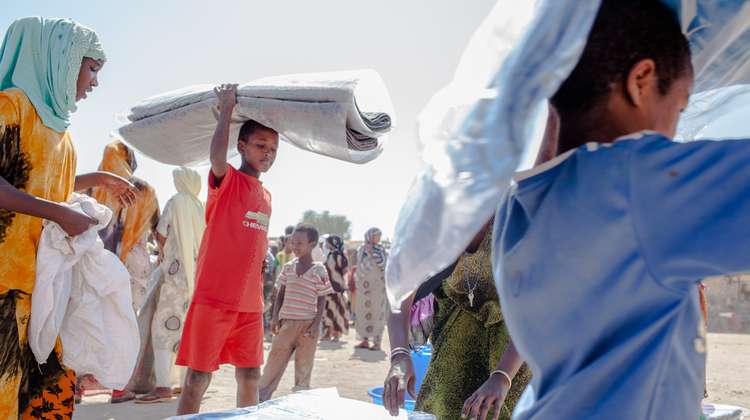 Kinder in einem Flüchtlingscamp werden bei einer Verteilung mit Decken und Kanistern versorgt